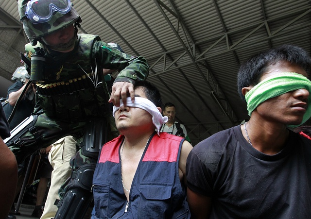Thai army soldier stands guard over handcuffed detainees during an operation to evict anti-government "red shirt" protesters from their encampment in Bangkok